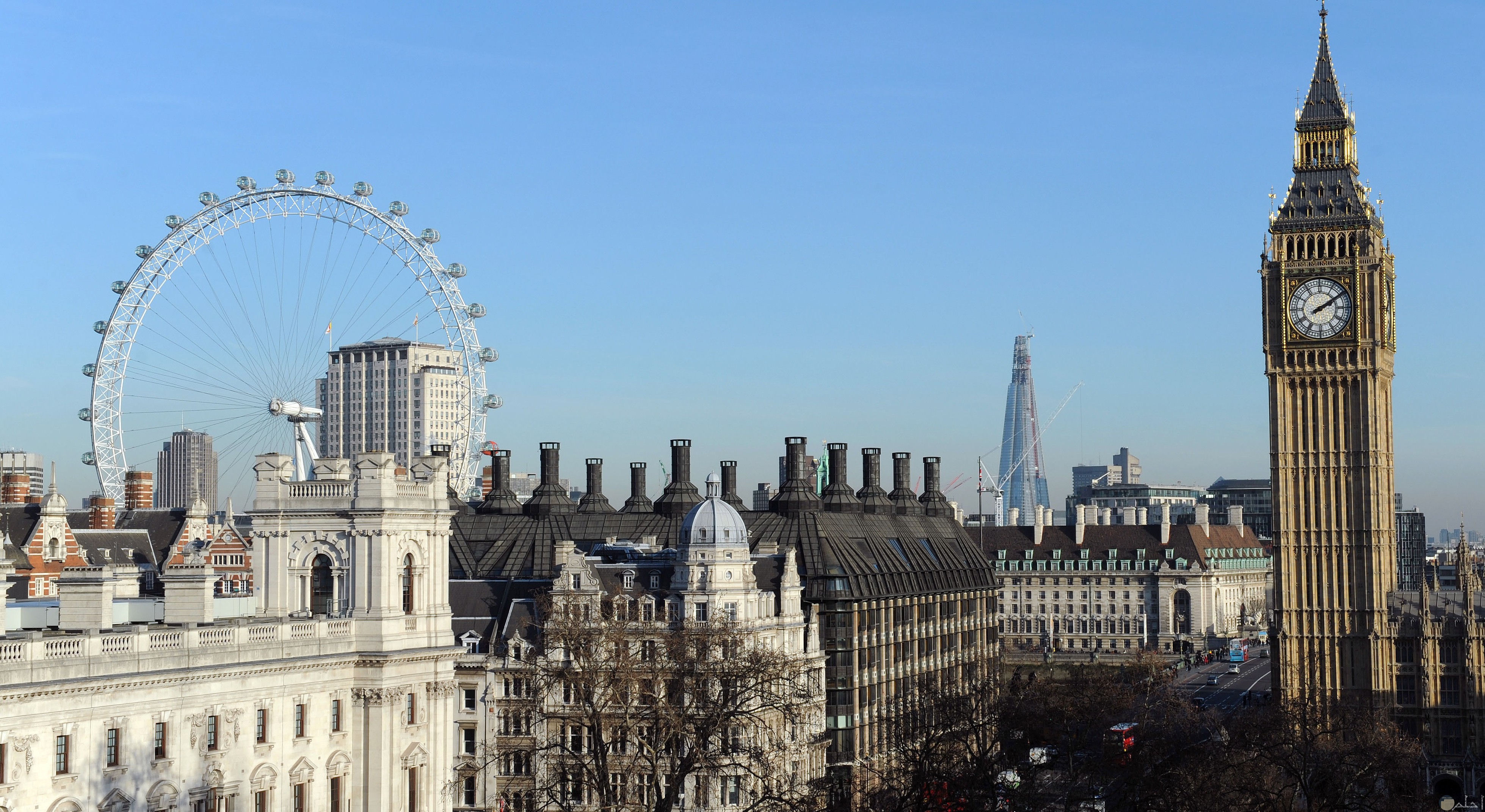 صورة تظهر الساعة المشهورة بلندن وعجلة عين لندن الضخمة بوقت النهار