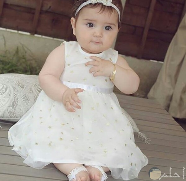 صورة جميلة جدا لبنت صغيرة جالسة ترتدي فستان أبيض حلو