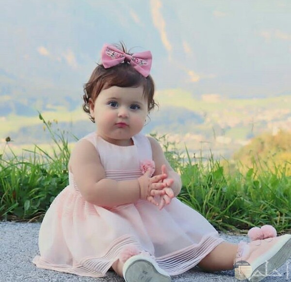 صورة جميلة جدا لبنت صغيرة جالسة علي الأرض ترتدي فستان وردي حلو