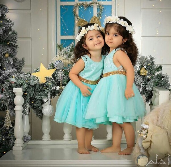 صورة جميلة جدا لبنتين صغار ترتدي كل منهن فستان لبني حلو مع طوق من الورد علي رأسيهما