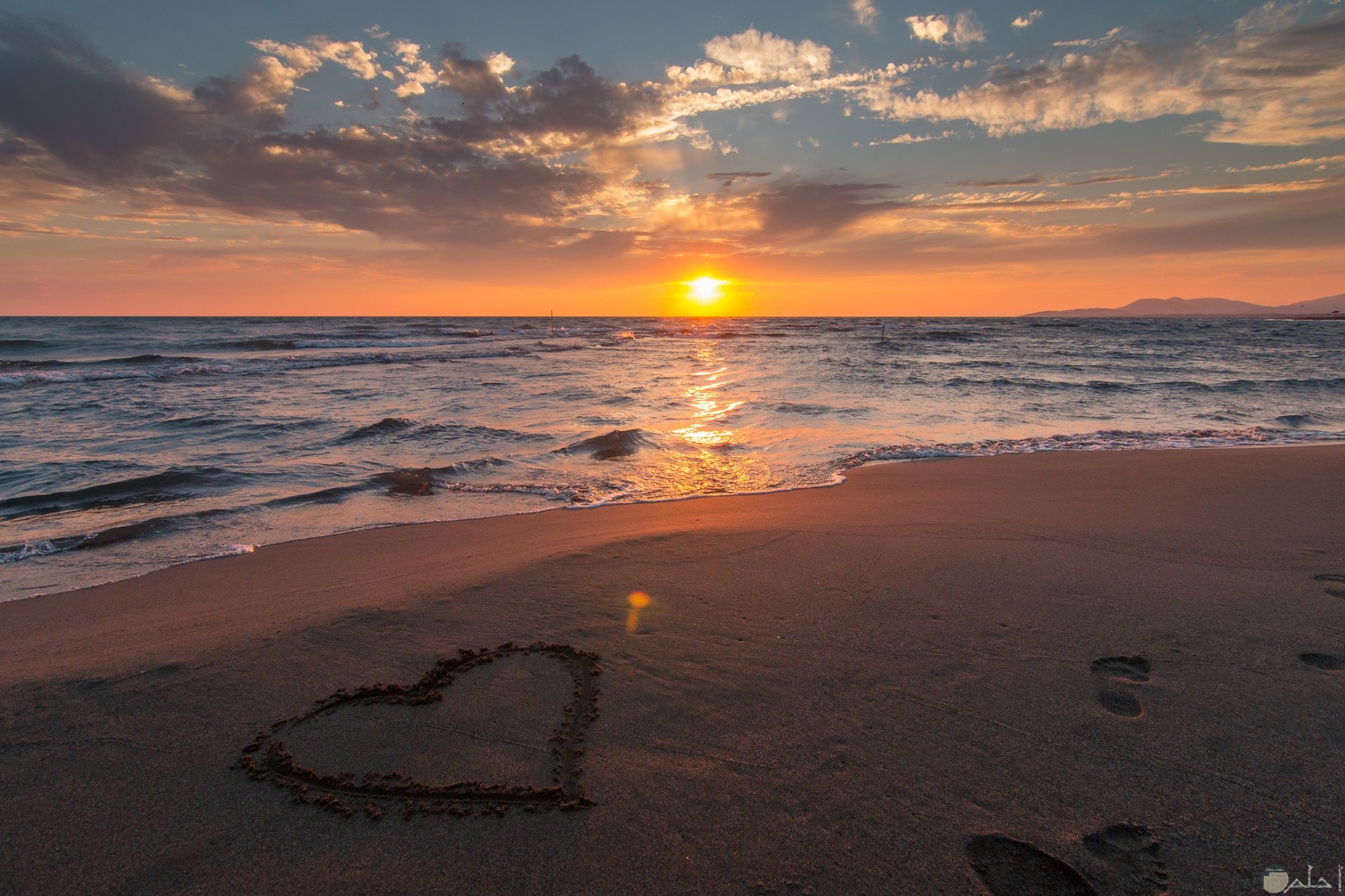 صورة جميلة لقلب مرسوم علي رمال الشاطئ بجانب البحر وقت الغروب