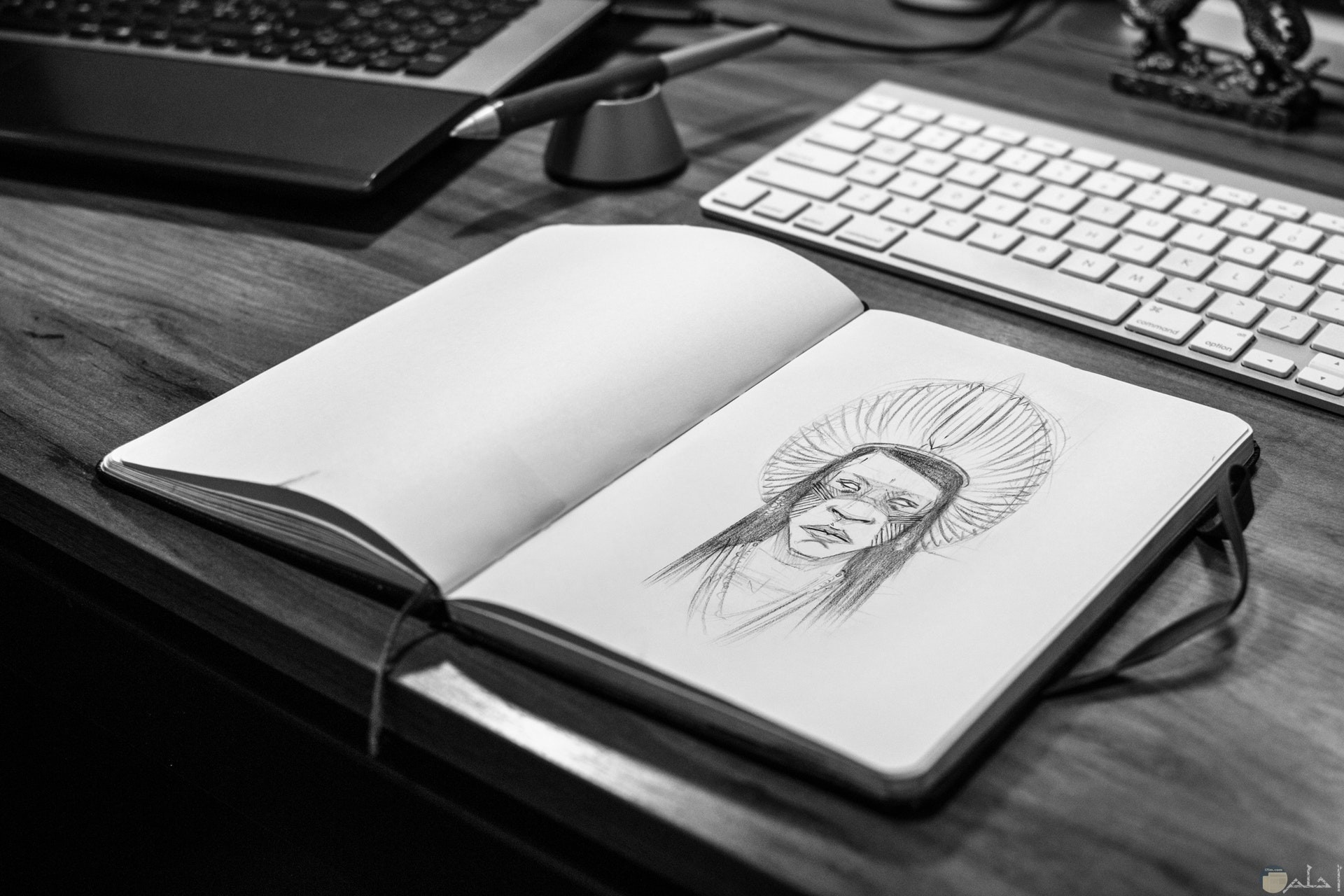 صورة لرسمة رجل من الهنود الحمر علي دفتر بجانبه لوحة مفاتيح كمبيوتر وقلم