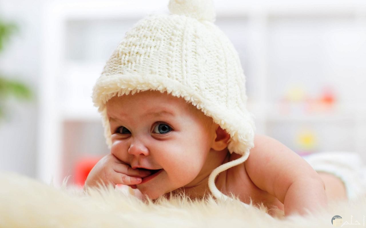 برائة الاطفال- طفل صغير بيضحك لابس طقية صوف بيضاء.