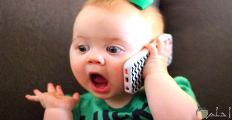طفلة جميلة تمسك هاتف محمول و كأنها تتحدث بيه.